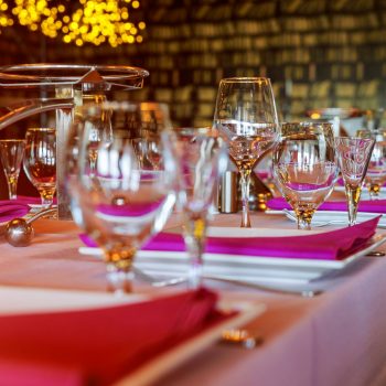 Glasses, flower fork, knife served for dinner in restaurant with cozy interior